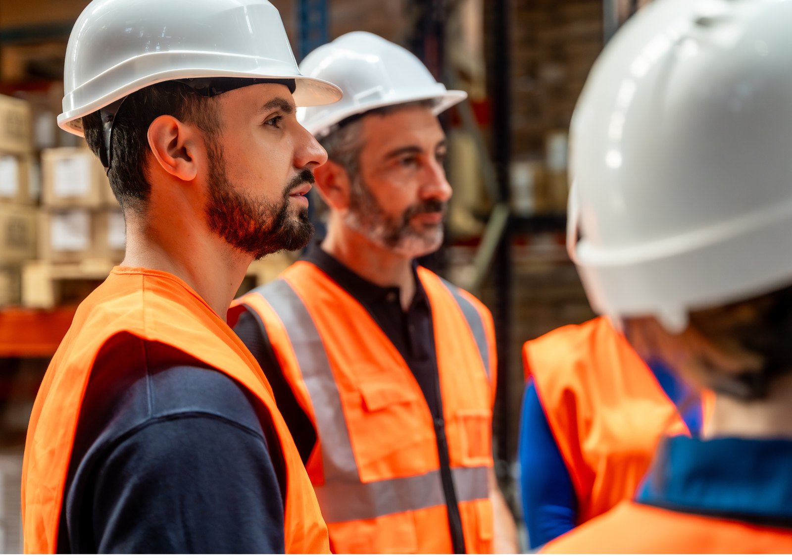 Trois professionnels équipés de casques et gilets haute visibilité échangent sur un site industriel
